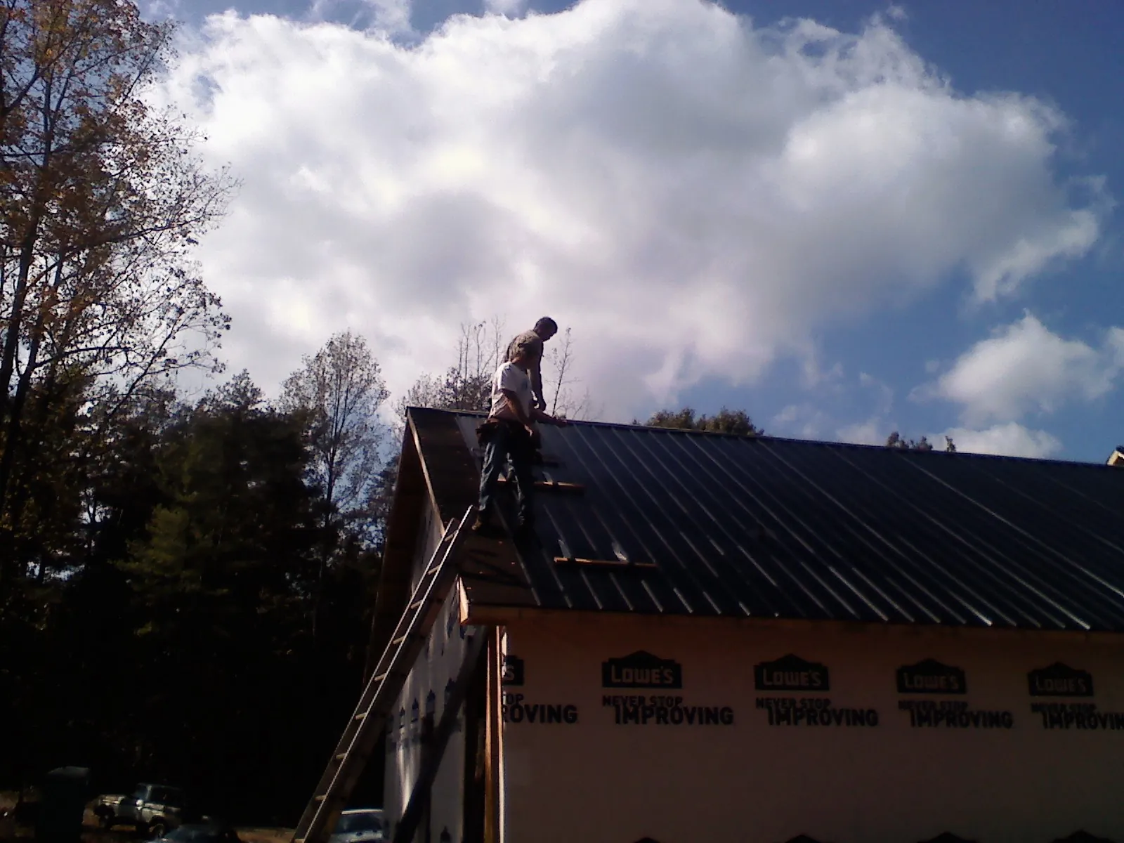 Roofer fastening dark metal panels high against a cloudy sky, from a Roof Inspection job in Laurel
